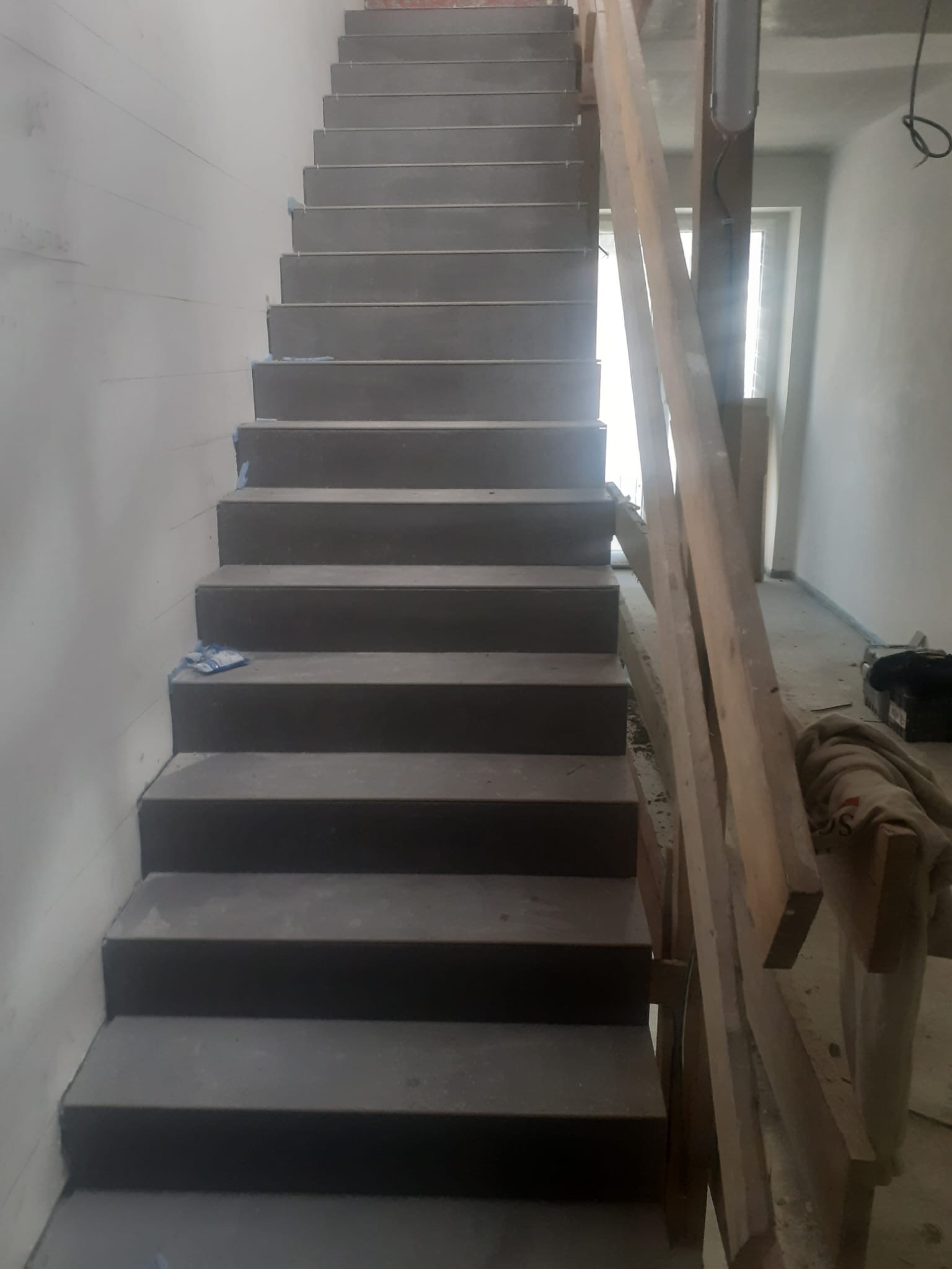 Surowe, betonowe schody w trakcie budowy, widoczne drewniane podpory, ściany w stanie surowym. Kąt ujęcia od dołu, ukazujący perspektywę schodów w górę.