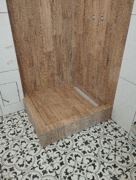 Nowoczesny brodzik wyłożony płytkami imitującymi drewno, z odpływem liniowym i dekoracyjną podłogą w czarno-białe wzory.