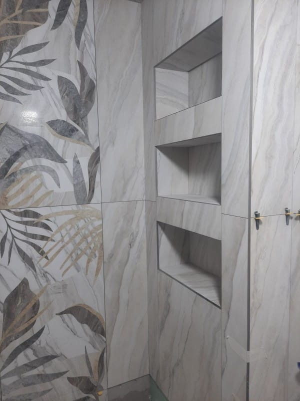 Wykończona ściana z płytek imitujących marmur z motywem roślinnym i wnękami. Widoczne krzyżyki dystansowe, co wskazuje na świeżo zakończone prace.