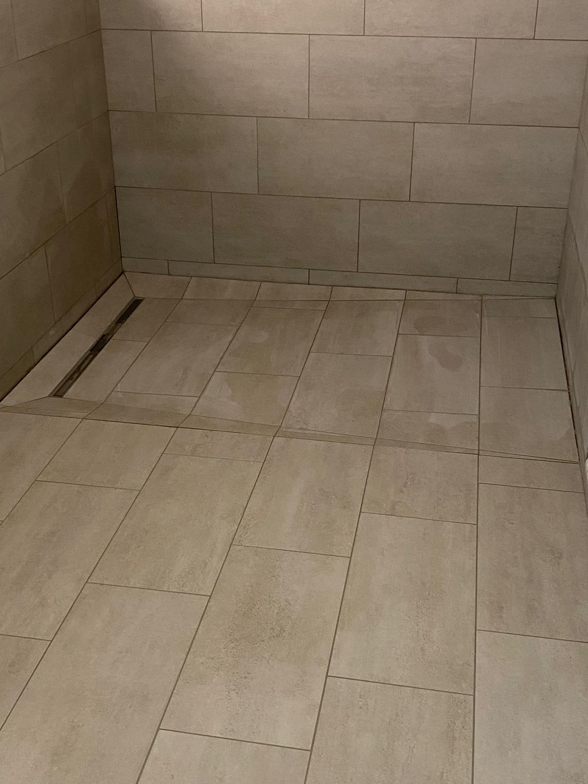 Nowoczesna kabina prysznicowa z beżowymi płytkami i odpływem liniowym, minimalistyczny design, neutralna kolorystyka.