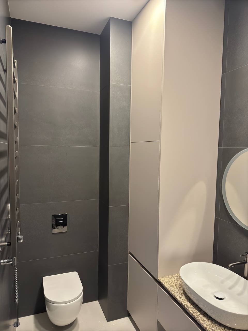 Elegancka łazienka w szarościach: płytki wielkoformatowe, minimalistyczna umywalka nablatowa i grzejnik drabinkowy. Nowoczesne wykończenie z dbałością o detale.