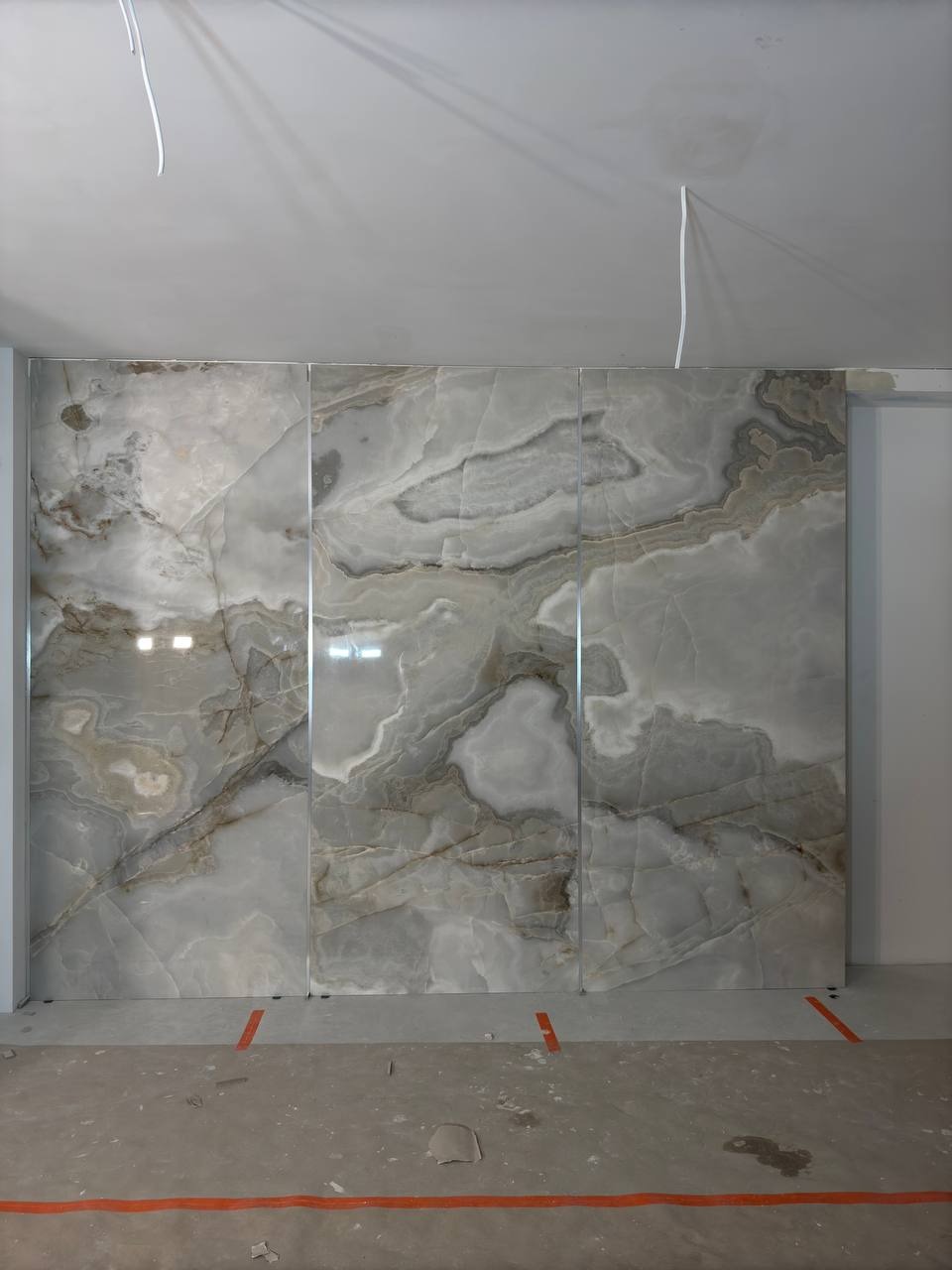 Ściana wyłożona wielkoformatowymi płytami imitującymi marmur w odcieniach szarości i bieli, z widocznymi spoinami i niedokończonym sufitem.