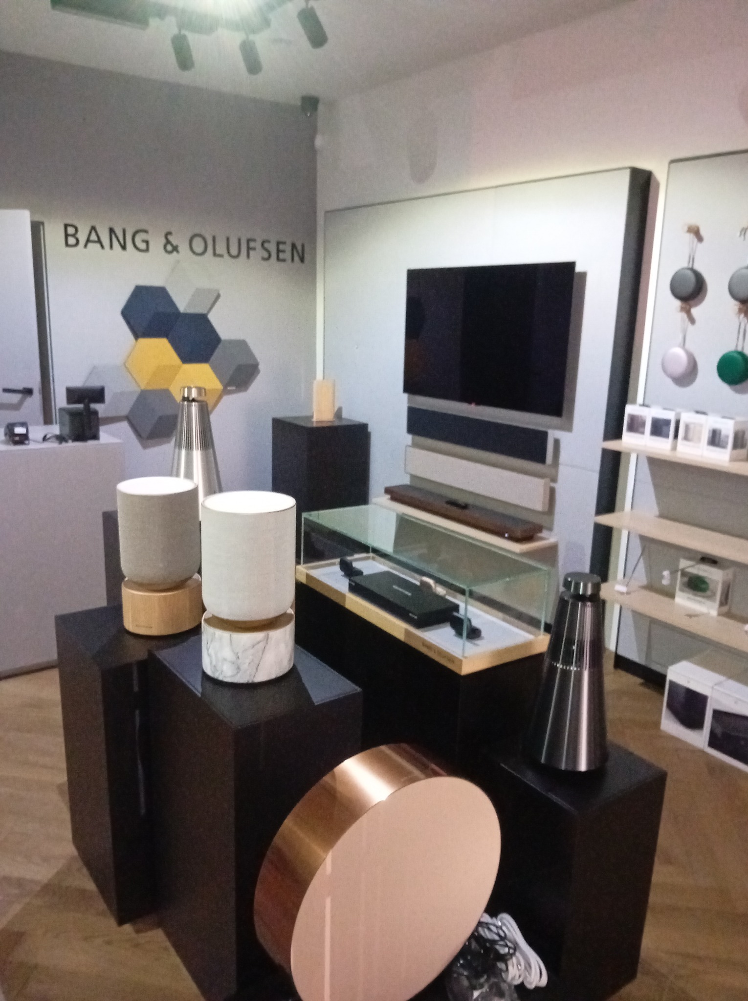 Salon Bang & Olufsen: ekspozycja sprzętu audio z głośnikami na postumentach, TV na ścianie i dekoracyjnymi panelami akustycznymi w tle.