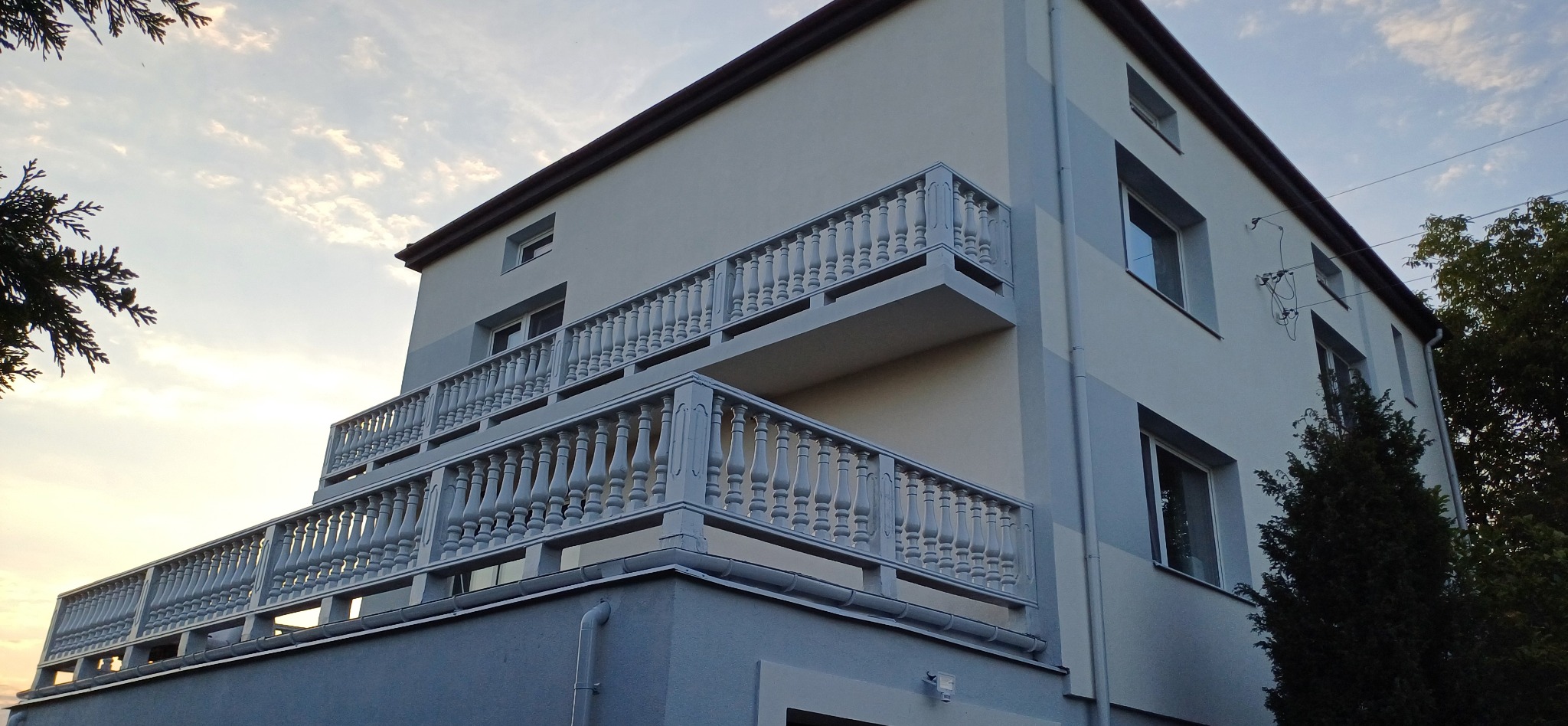 Dwupiętrowy dom z balkonami z balustradami w stylu retro, pomalowany na pastelowe kolory. Widok z dołu na elewację i okna w pogodny dzień.