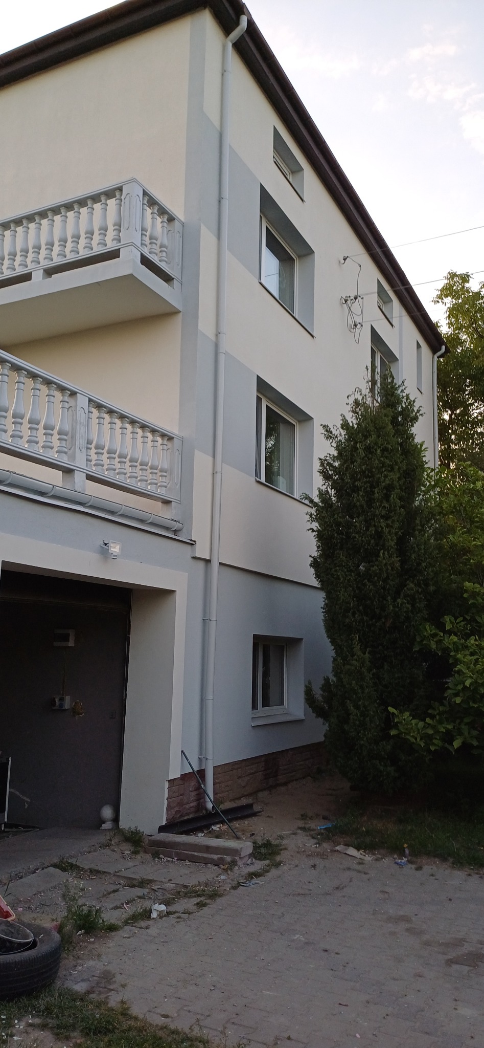 Dwukondygnacyjny dom po malowaniu elewacji z balkonami z białą balustradą. Widoczny fragment garażu i roślinność. Ujęcie z dołu, podkreślające wysokość budynku.