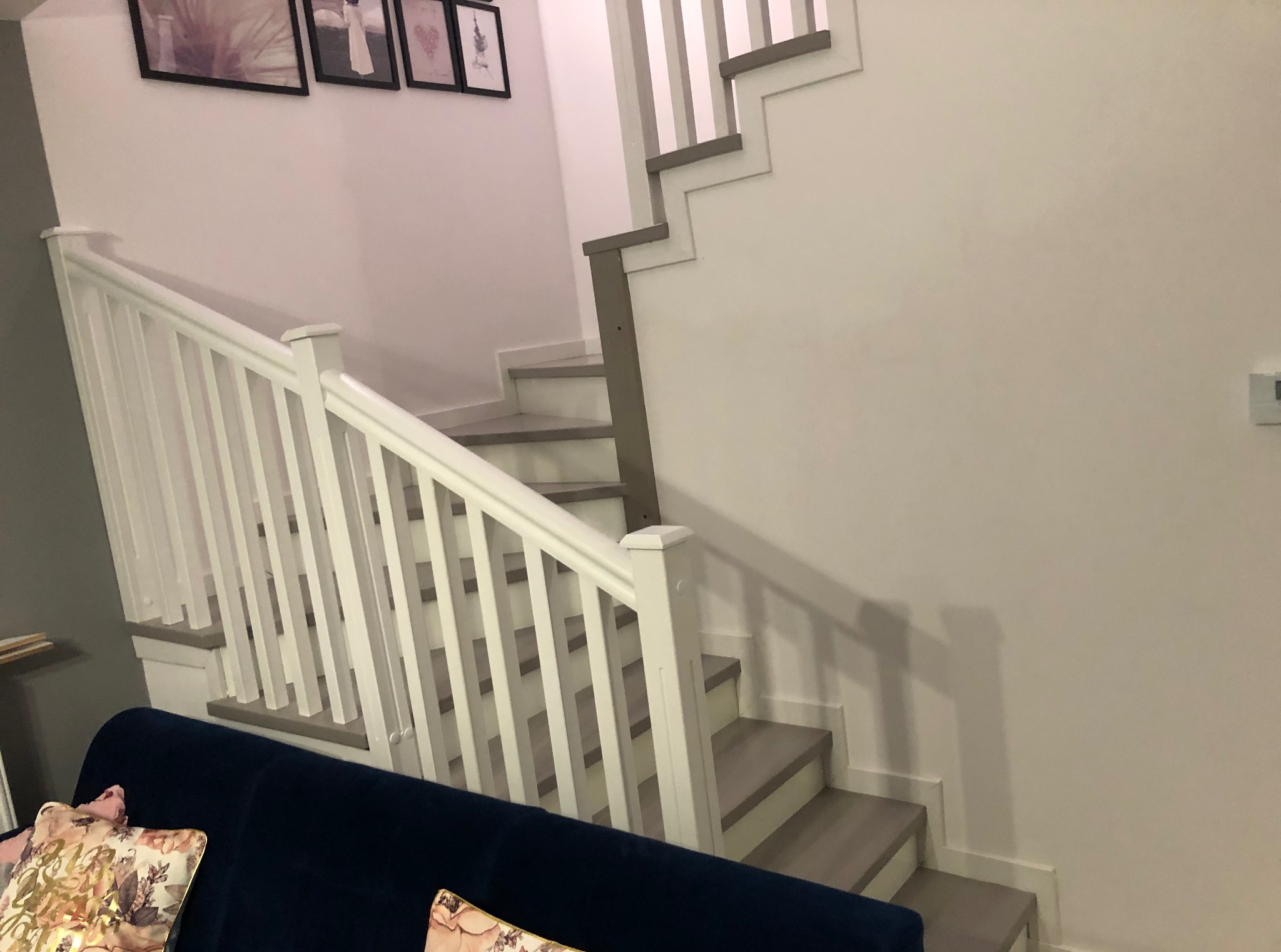 Nowoczesne schody z białymi balustradami i szarymi stopniami, widok z dołu, sofa w tle. Minimalistyczny design.