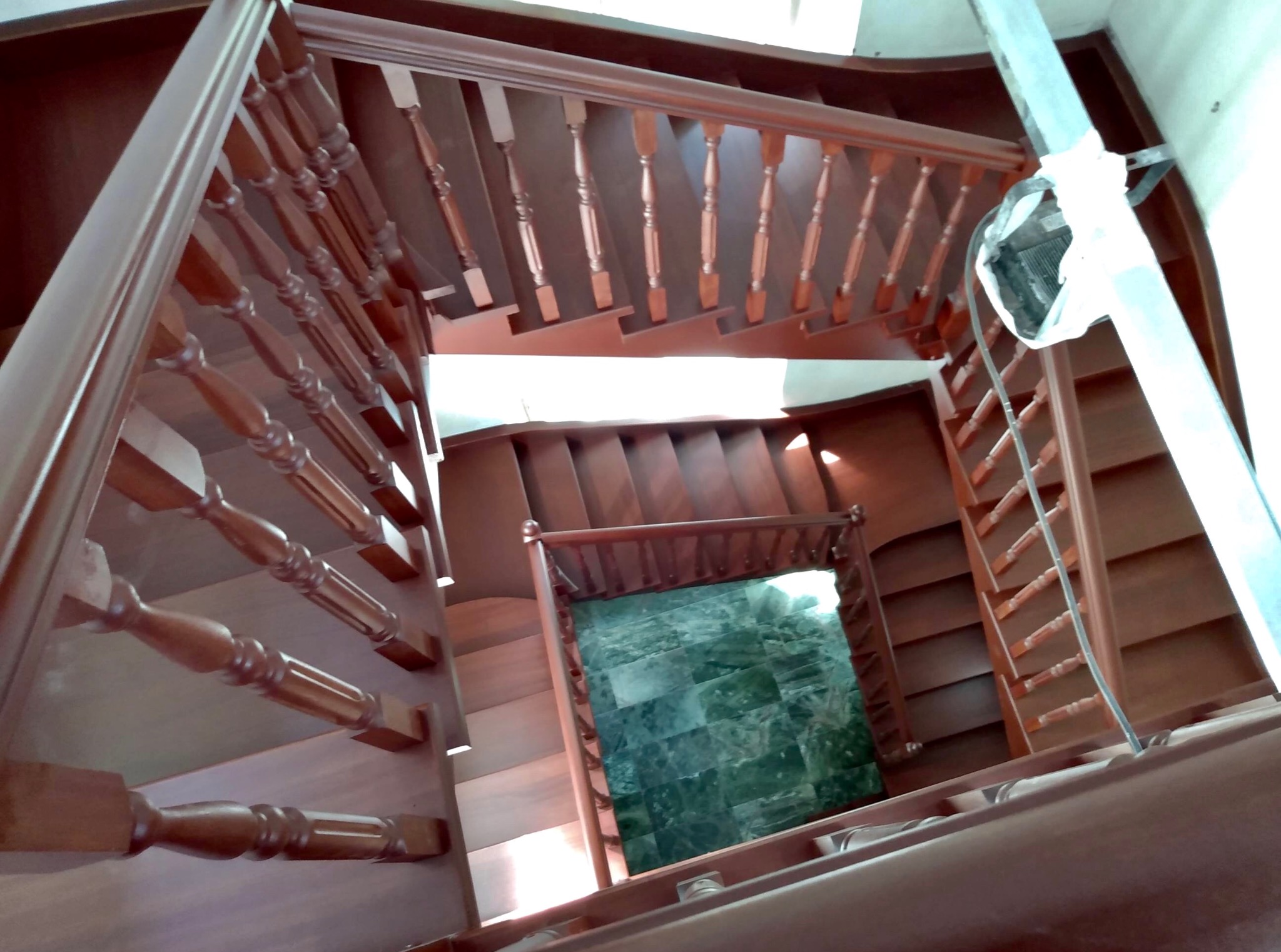 Drewniane schody z balustradą, widok z góry, w domu w Grodzisku Mazowieckim. Ciemne drewno, spiralny układ, widoczne stopnie i poręcze. Nietypowy kadr.