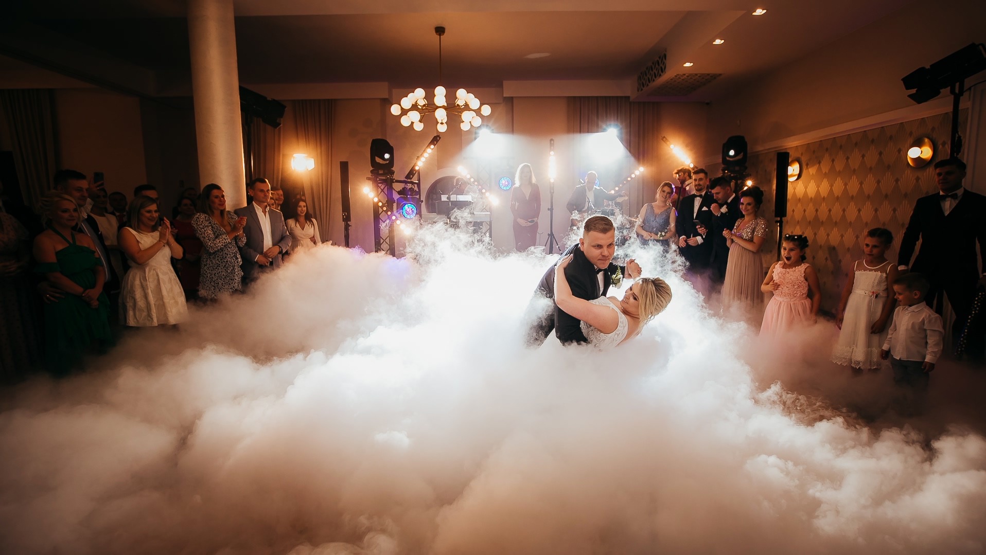 Pierwszy taniec pary młodej w Otwocku, otoczonej dymem scenicznym i oświetleniem, z zespołem muzycznym w tle i gośćmi weselnymi.
