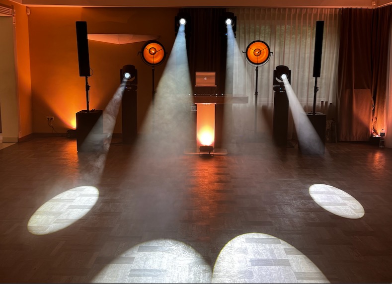 Scena oświetlona reflektorami i lampami, z laptopem na biurku. Pomieszczenie z parkietem, kurtyna w tle. Gotowość do występu.