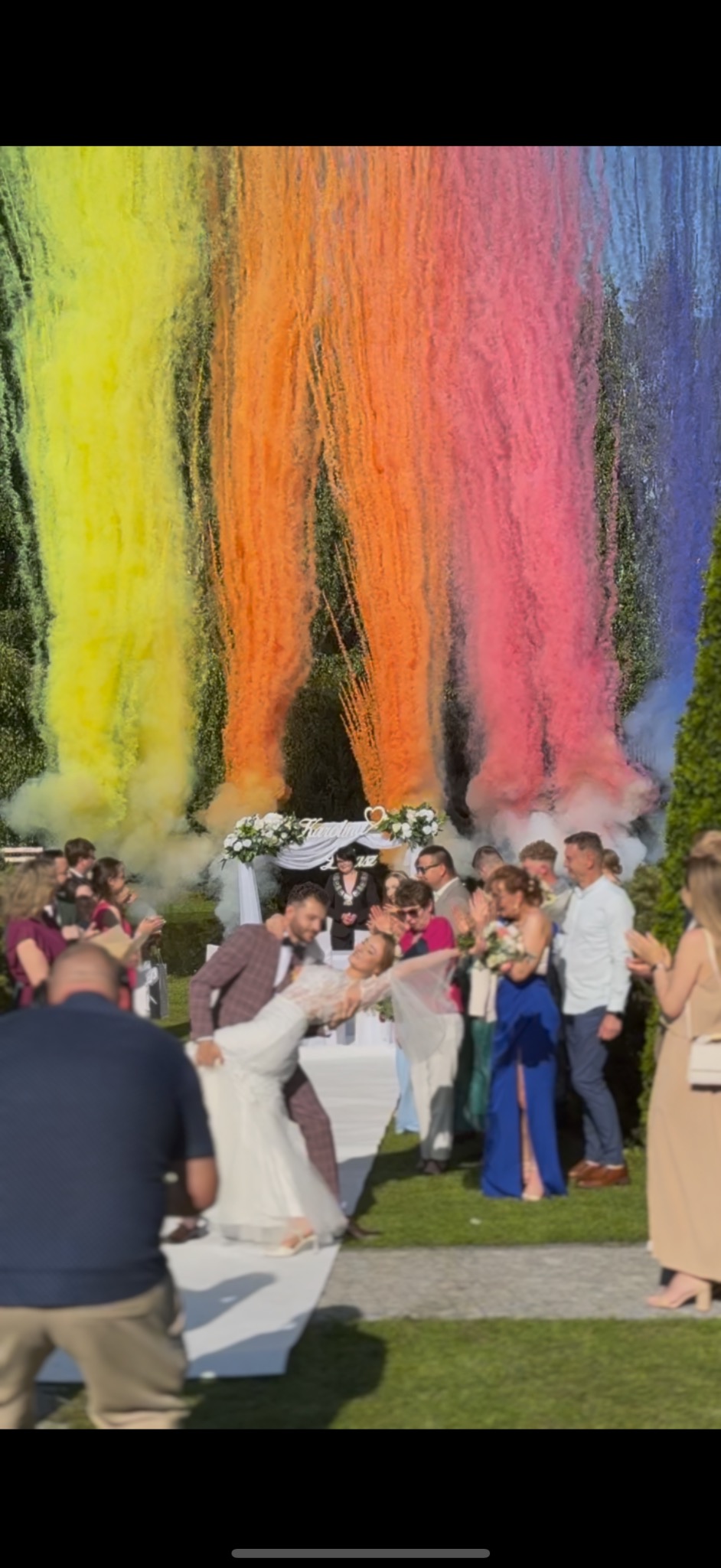 Para młoda tańczy na ślubie, w tle kolorowe fontanny dymne i goście. Ujęcie z bliska, uchwycone emocje i radość chwili.