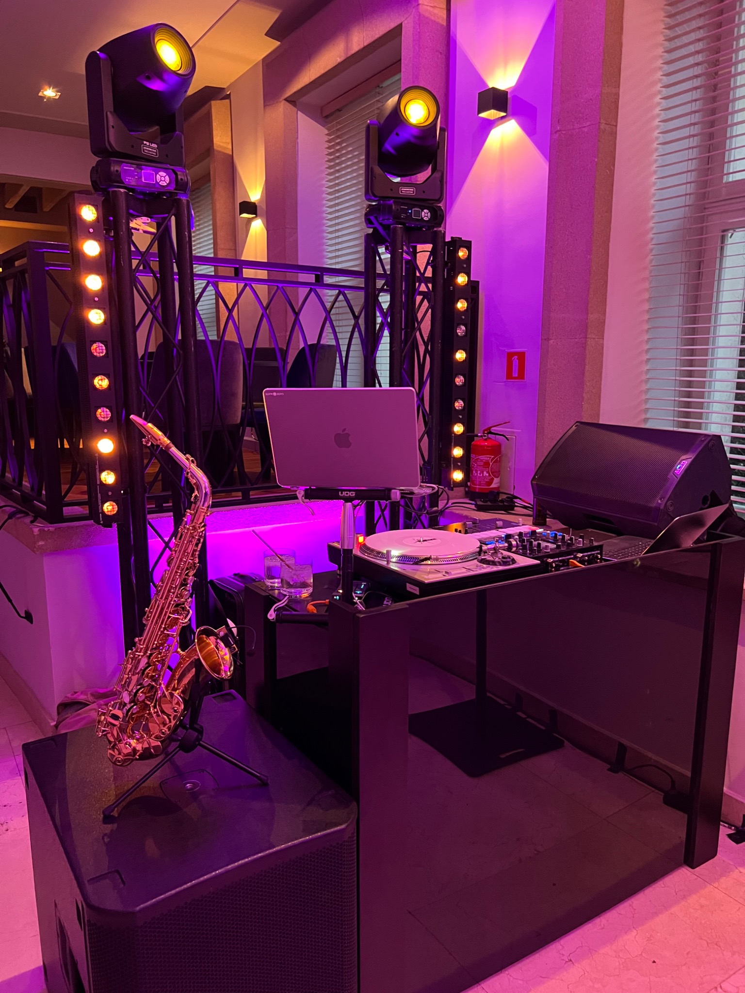Scena z saksofonem, sprzętem DJ-skim i oświetleniem w fioletowej tonacji. Laptop na statywie. Gotowość do występu muzycznego.
