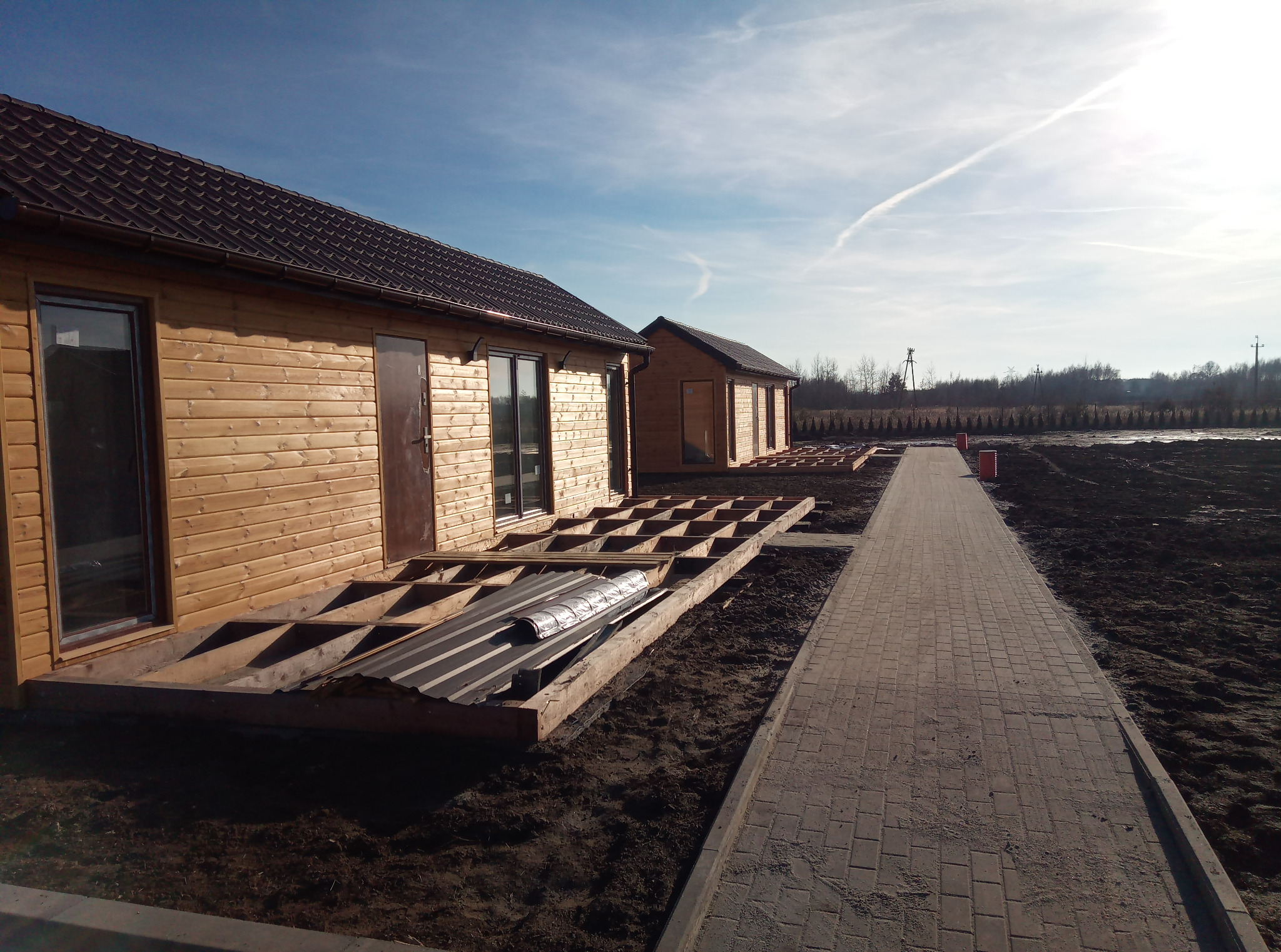 Budowa drewnianych domków letniskowych z tarasami w trakcie realizacji. Widoczny szkielet tarasu, kostka brukowa i elementy konstrukcyjne.