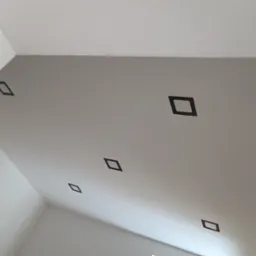 Szary sufit z zamontowanymi, kwadratowymi oprawami oświetleniowymi w kolorze czarnym, rozmieszczonymi w rzędzie, widok z dołu.