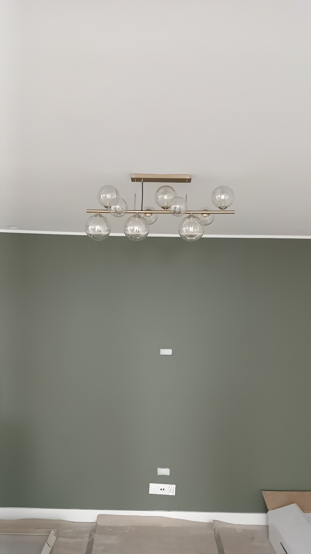 Zamontowana lampa sufitowa z kulistymi kloszami w nowoczesnym wnętrzu. Zielona ściana i biały sufit. Widoczne gniazdka elektryczne.