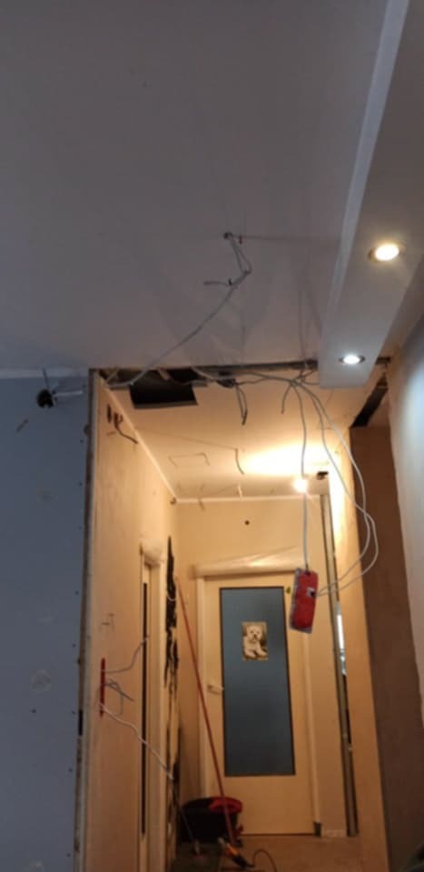Remont korytarza w trakcie: widoczne kable, otwory w suficie, ściany z płyt kartonowo-gipsowych. Etap instalacji elektrycznej i przygotowania do wykończenia.