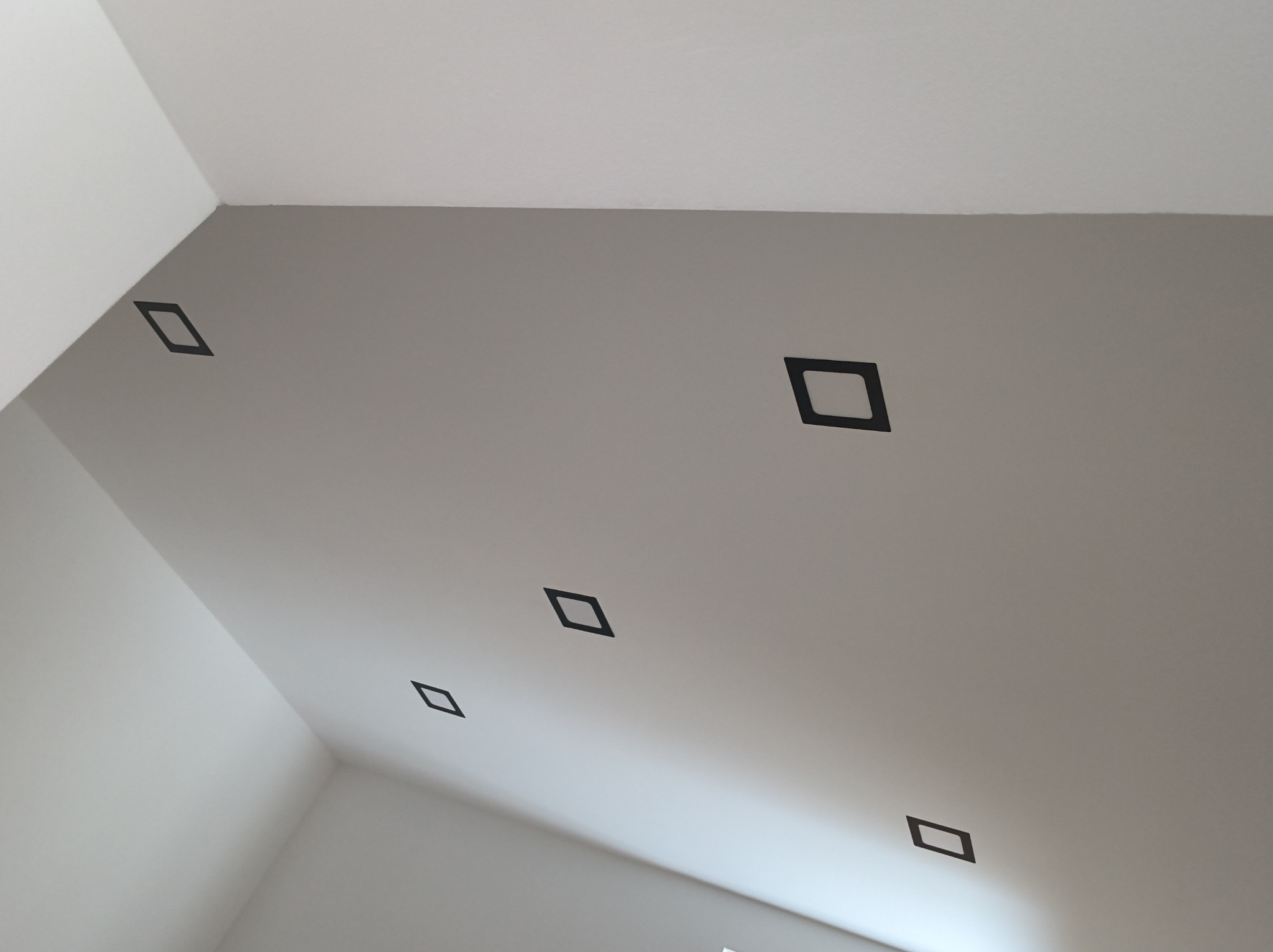 Szary sufit z zamontowanymi, kwadratowymi oprawami oświetleniowymi w kolorze czarnym, rozmieszczonymi w rzędzie, widok z dołu.