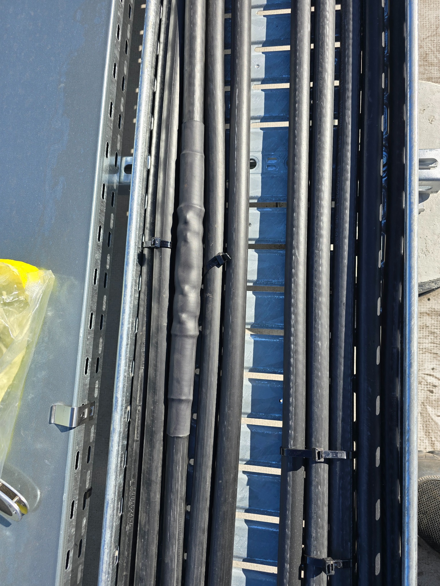 Kable elektryczne w metalowej korycie kablowej, zabezpieczone opaskami zaciskowymi. Widoczne złącze kablowe w gumowej osłonie.