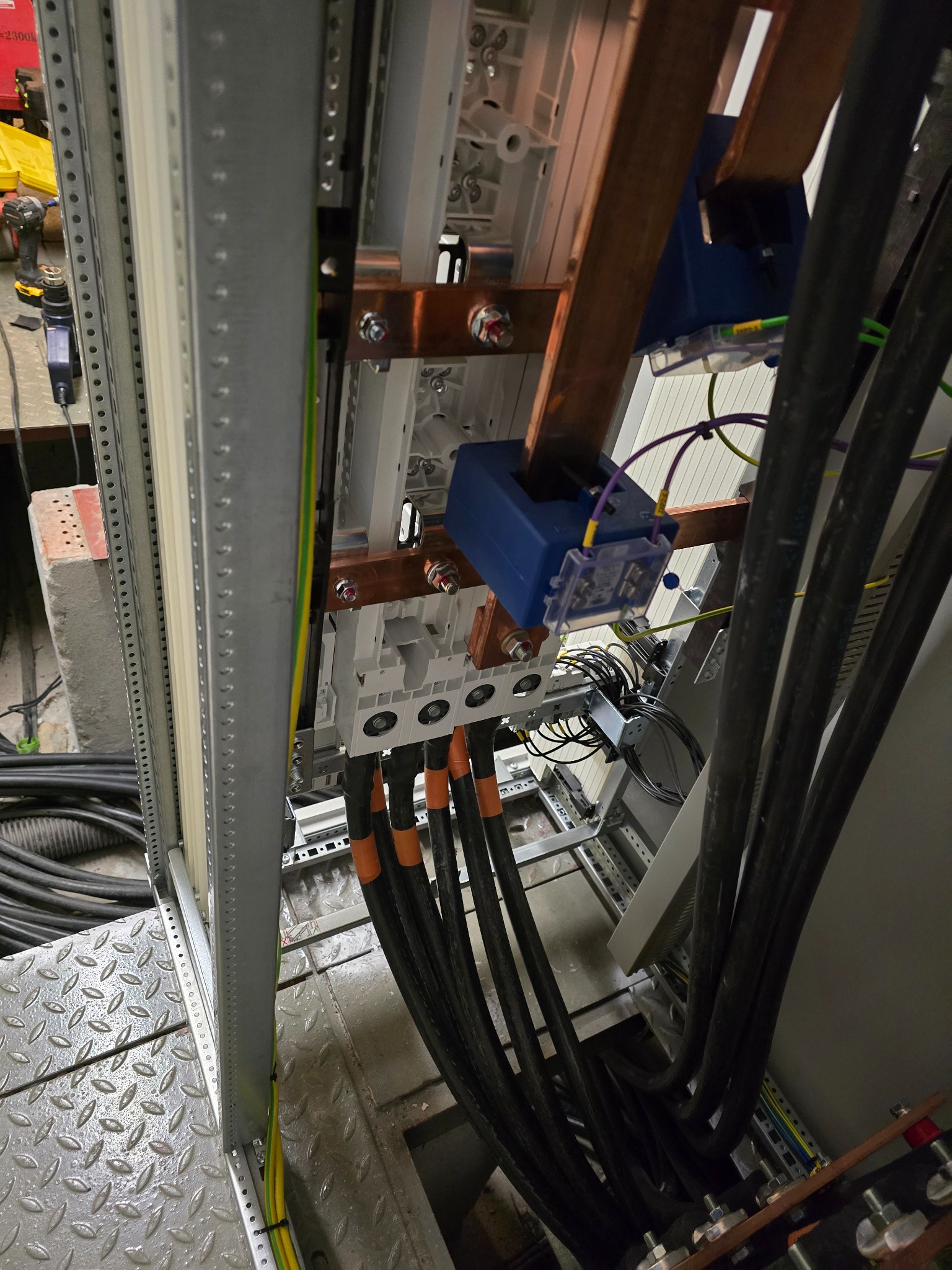 Rozdzielnia elektryczna w trakcie montażu: kable zasilające, szyny miedziane, zabezpieczenia. Widoczne elementy konstrukcyjne i narzędzia monterskie w tle.