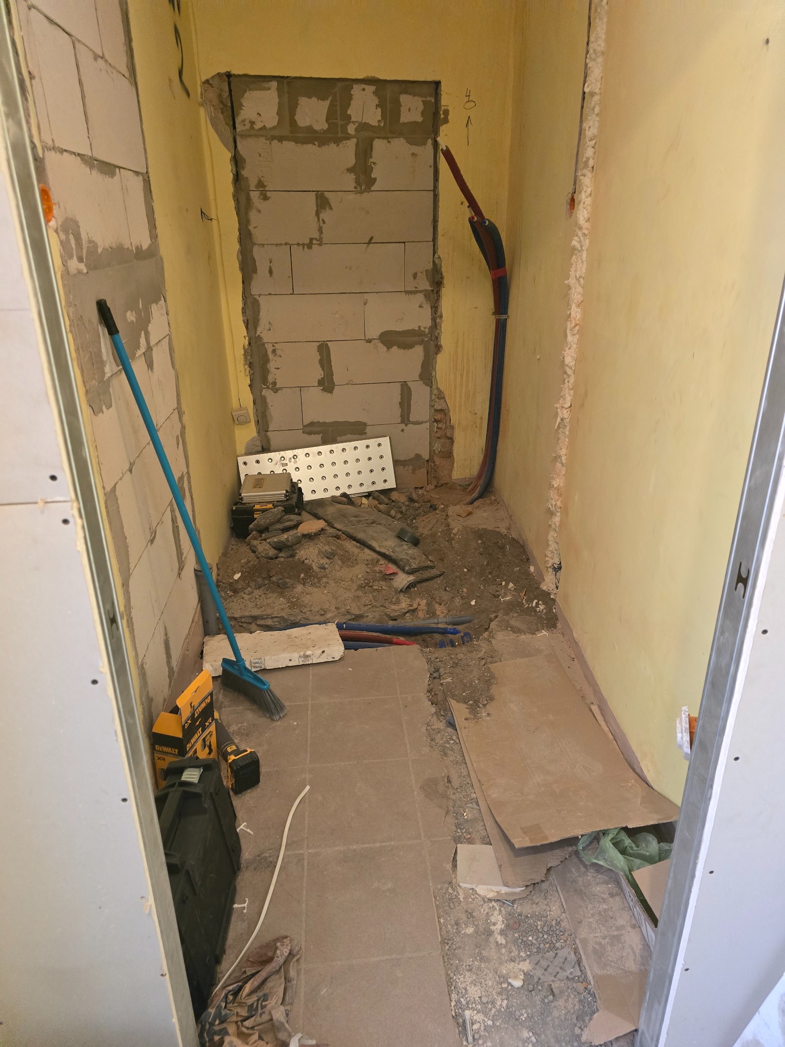 Wnętrze w trakcie remontu: widoczne narzędzia, materiały budowlane i fragmenty instalacji. Ściany w surowym stanie, przygotowane do dalszych prac wykończeniowych.
