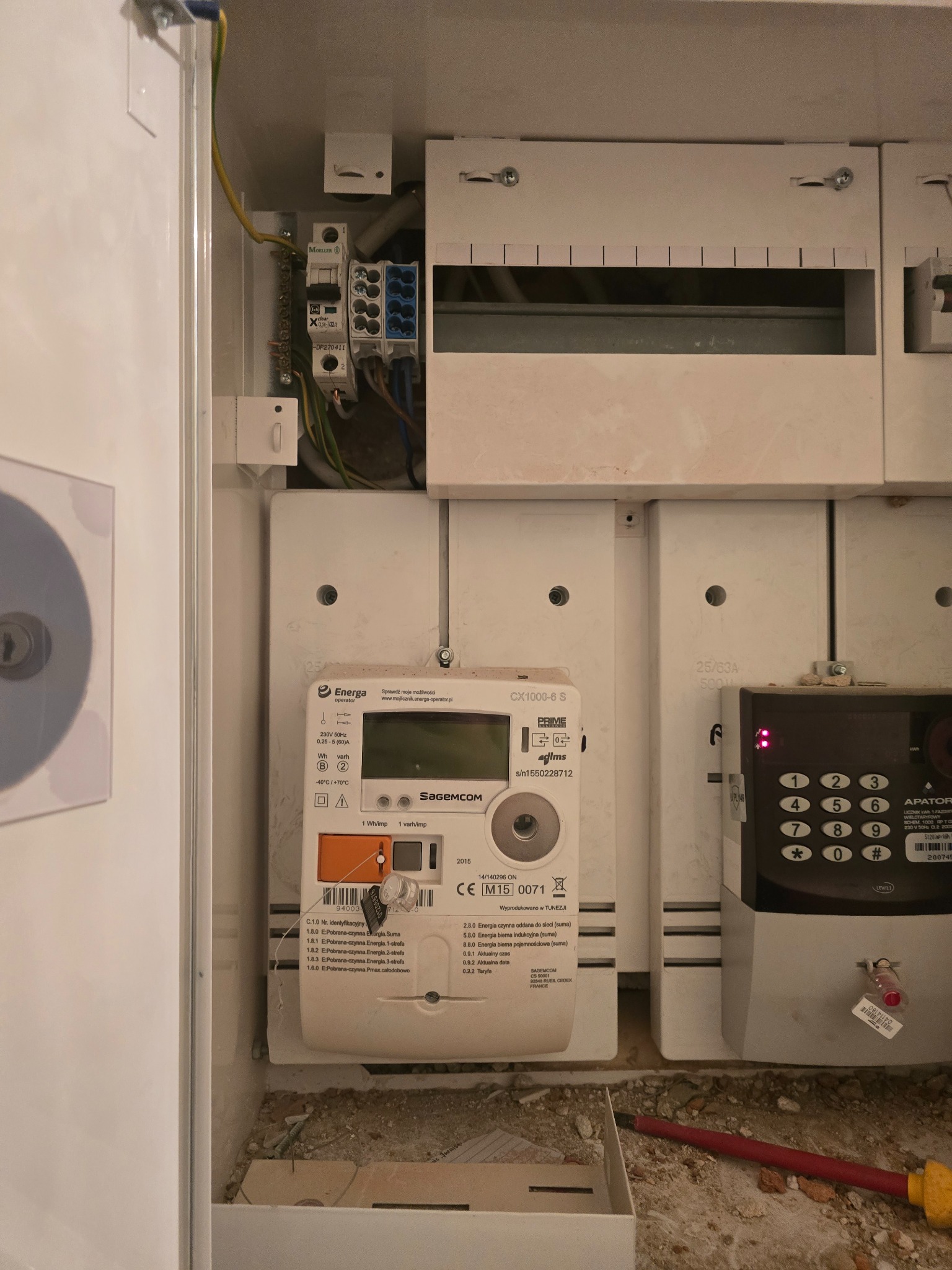 Szafka elektryczna z zamontowanym licznikiem energii Energa i zabezpieczeniami Moeller. Widoczne przewody i elementy instalacji elektrycznej.