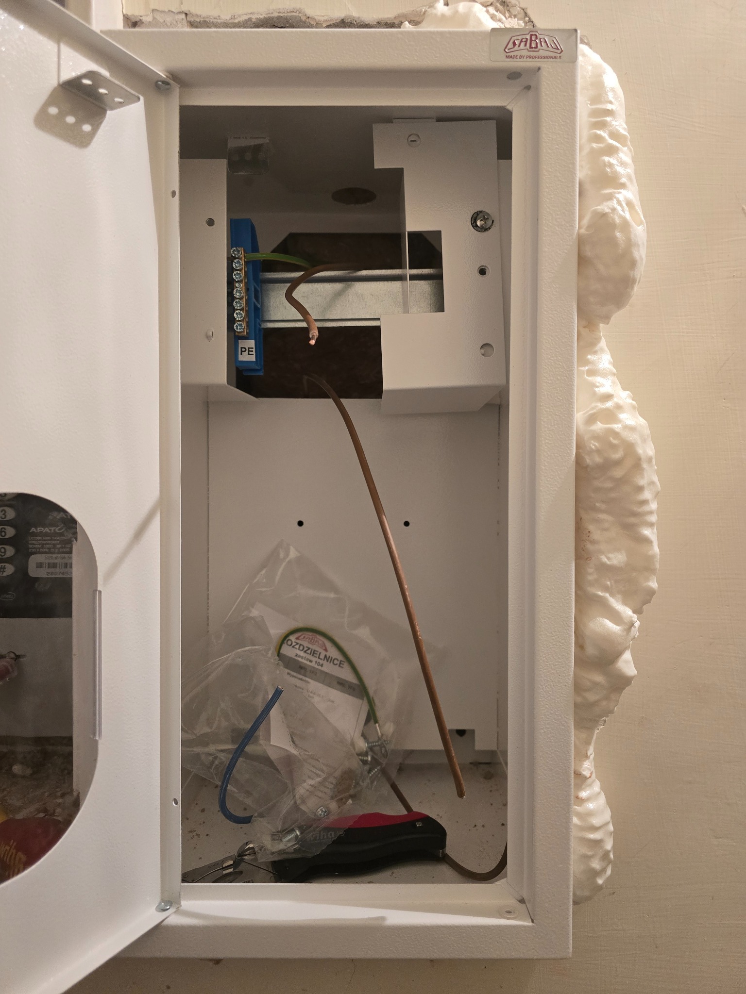 Otwarta skrzynka elektryczna z przewodami i narzędziami w Bydgoszczy. Widoczna piana montażowa uszczelniająca obudowę. Elementy instalacji wewnątrz.