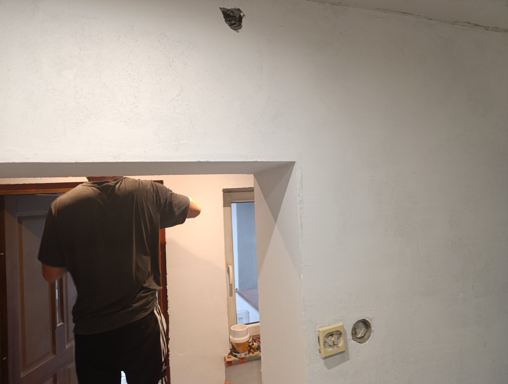 Tynkowanie ściany wewnątrz budynku z widocznymi puszkami elektrycznymi i otworem w suficie. Prace wykończeniowe w trakcie realizacji.