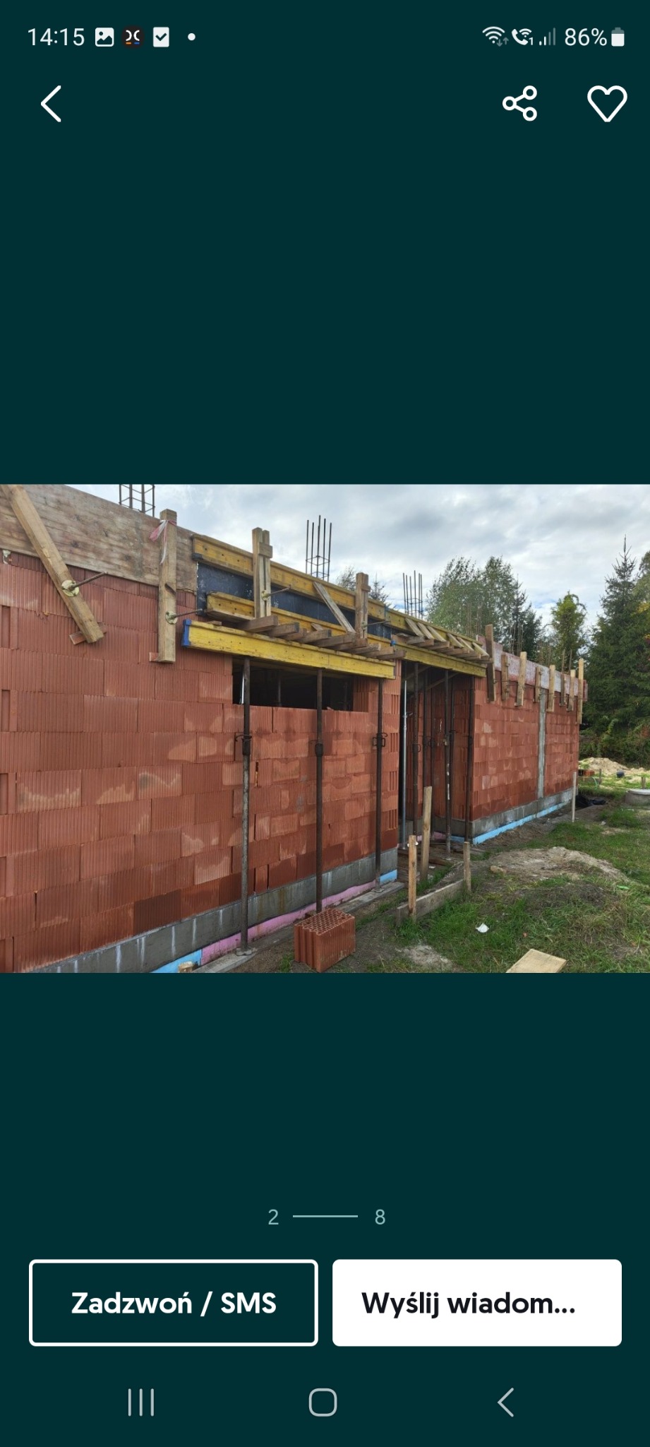 Budowa domu z czerwonej cegły: ściany w trakcie murowania, widoczne podpory, drewniane szalunki i izolacja fundamentów. Etap wznoszenia ścian.