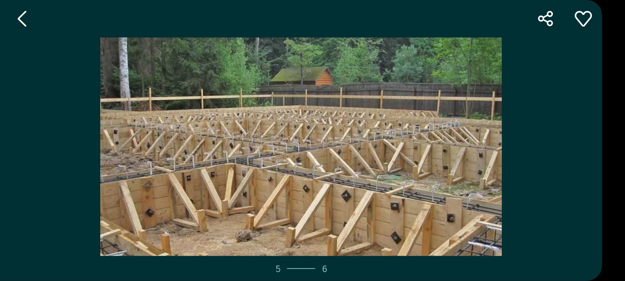 Szeroki kadr: drewniany szalunek fundamentów zbrojonych stalą na działce budowlanej, w tle drzewa i ogrodzenie z desek. Konstrukcja przygotowana do zalania betonem.