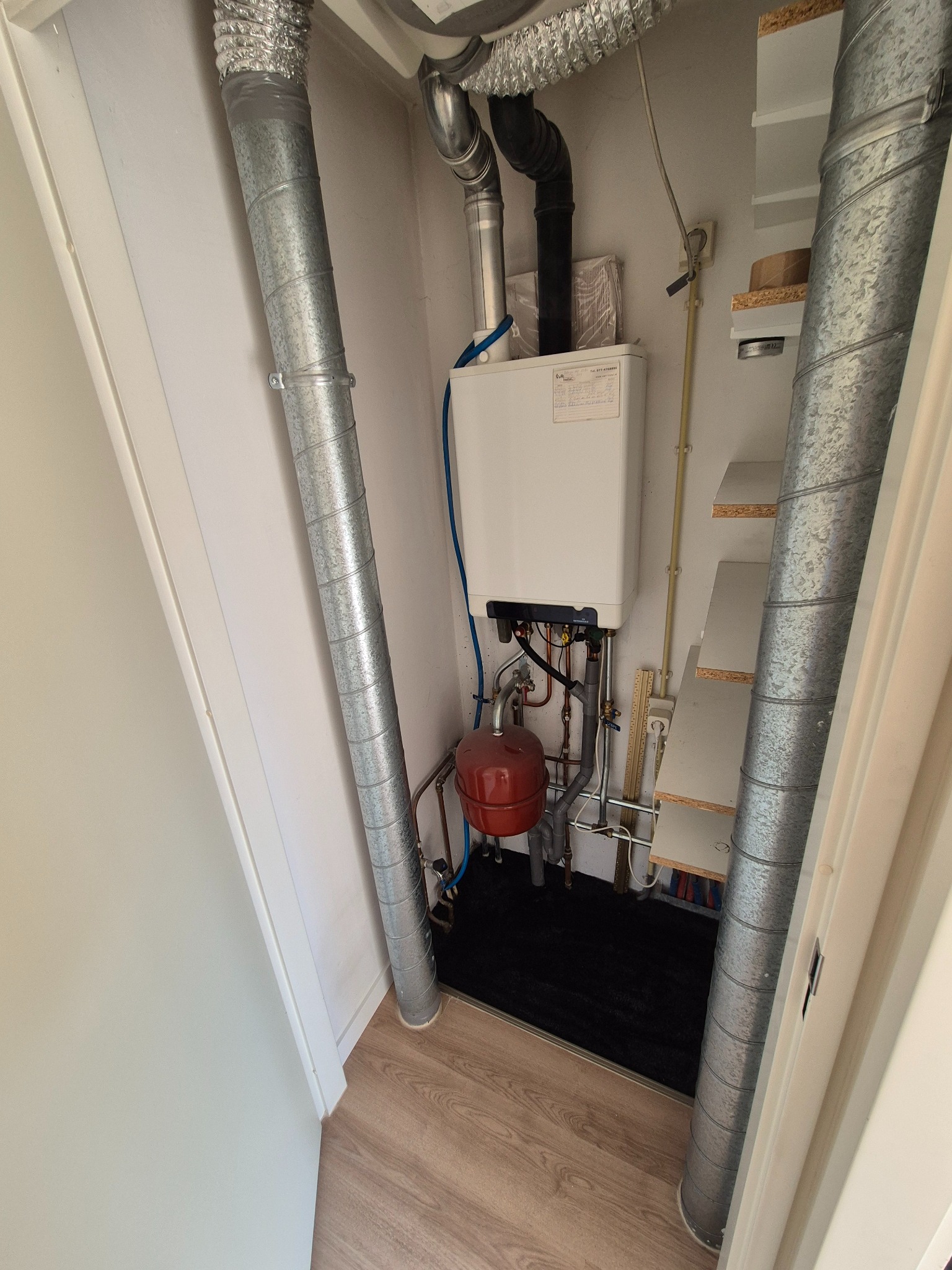 Wnętrze szafy z piecem gazowym, rurami wentylacyjnymi i półkami. Widoczne elementy instalacji i wykończenia.