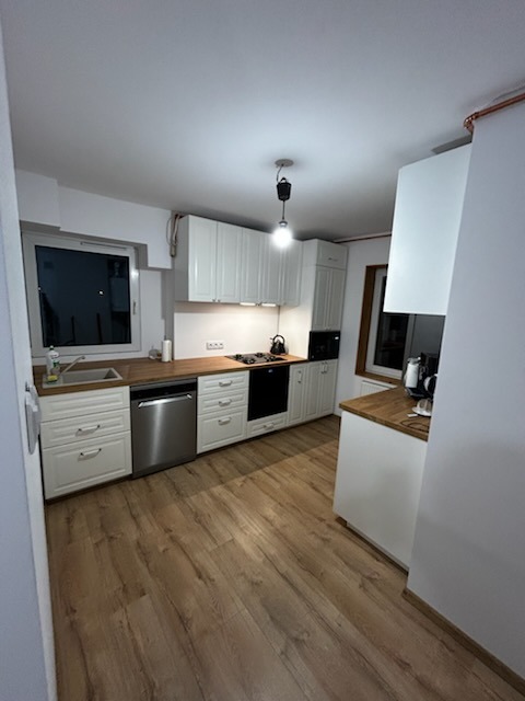 Jasna kuchnia w stylu skandynawskim po remoncie: białe szafki z drewnianym blatem, drewniana podłoga, okno z widokiem na nocne niebo. Minimalistyczny design.