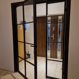 MAGIC FISH SPÓŁKA Z OGRANICZONĄ ODPOWIEDZIALNOŚCIĄ - Loftowe drzwi szklane z czarną ramą, częściowo otwarte, widok na wnętrze. Realizacja z Zaleszan.