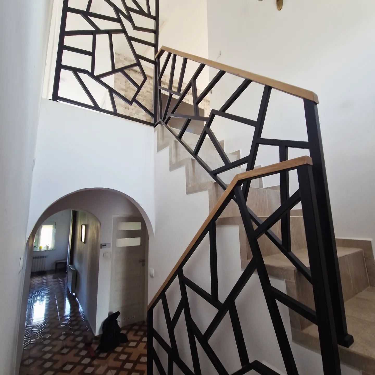 Nowoczesna balustrada schodowa z czarną, geometryczną konstrukcją i drewnianym poręczą, wzbogacona o ażurowy panel w górnej części schodów.