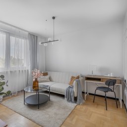 Adrian Tokarz Marketing - Jasne wnętrze salonu z parkietem w jodełkę, sofą, stolikiem kawowym i biurkiem. Stonowana kolorystyka, minimalistyczny design, dekoracyjne panele ścienne.