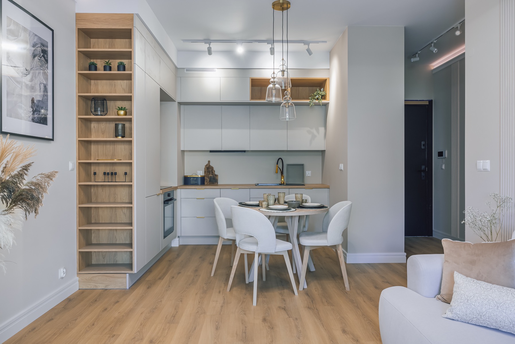 Jasne wnętrze: kuchnia z jadalnią w odcieniach szarości i drewna. Minimalistyczny design, okrągły stół z krzesłami, drewniana podłoga i regał z dekoracjami.