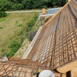 S bud dach - Zbrojenie dachu domu jednorodzinnego, widok z góry, narzędzia pracy w rogu. Konstrukcja z prętów stalowych na drewnianym szalunku, przygotowana do zalania betonem.