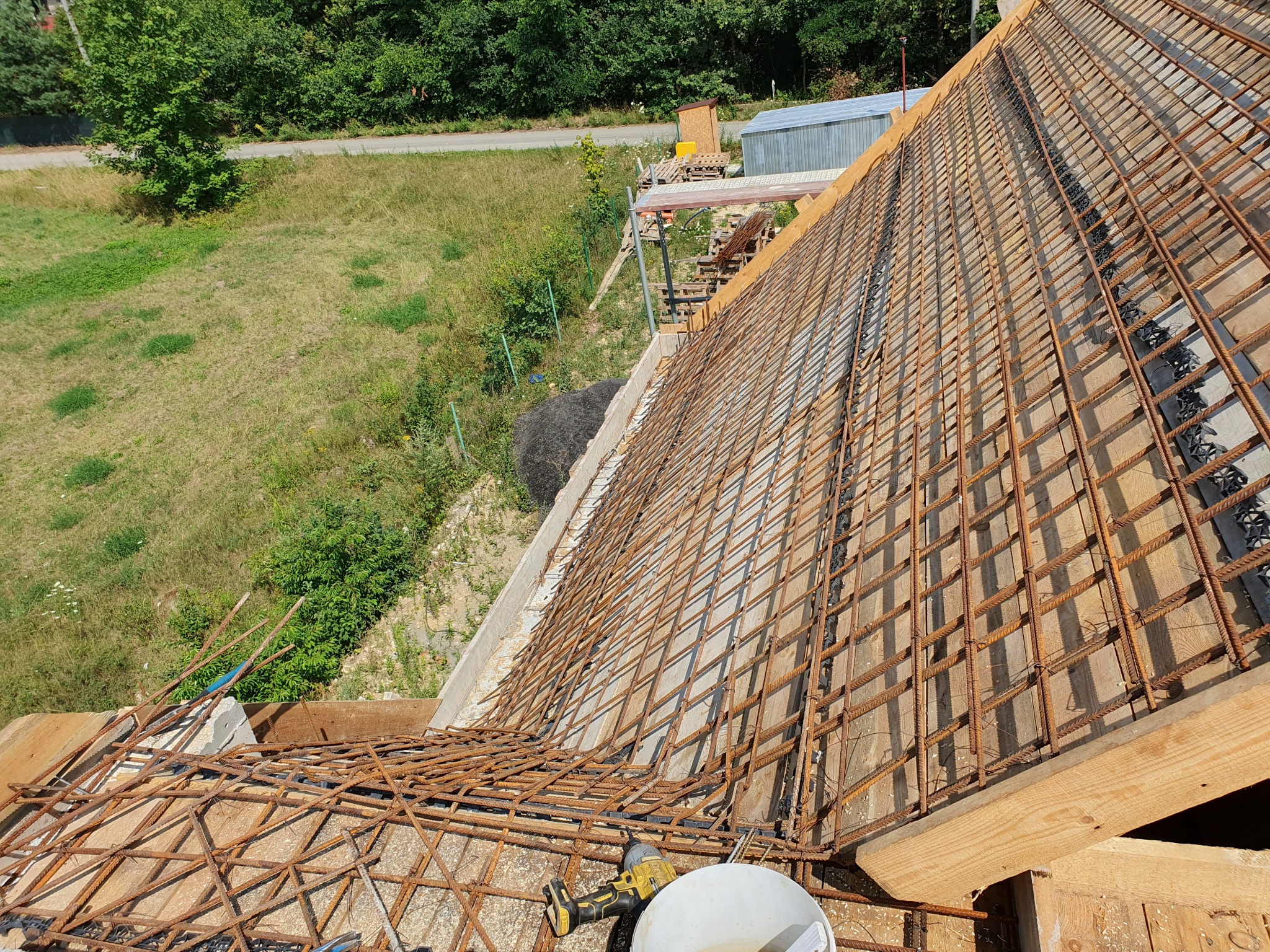 Zbrojenie dachu domu jednorodzinnego, widok z góry, narzędzia pracy w rogu. Konstrukcja z prętów stalowych na drewnianym szalunku, przygotowana do zalania betonem.