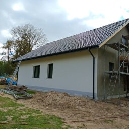 REMI-DEK PIOTR FRĄCKIEWICZ - Dom jednorodzinny w trakcie wykończenia: świeżo położona dachówka, ocieplona elewacja, widoczne rusztowania i drabina. Prace wykończeniowe w toku.