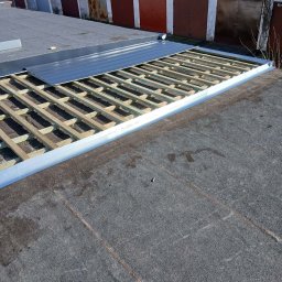 REMI-DEK PIOTR FRĄCKIEWICZ - Montaż drewnianej konstrukcji pod blachę na płaskim dachu budynku garażowego. Widoczne elementy mocujące i częściowo ułożona blacha. Prace dekarskie w toku.