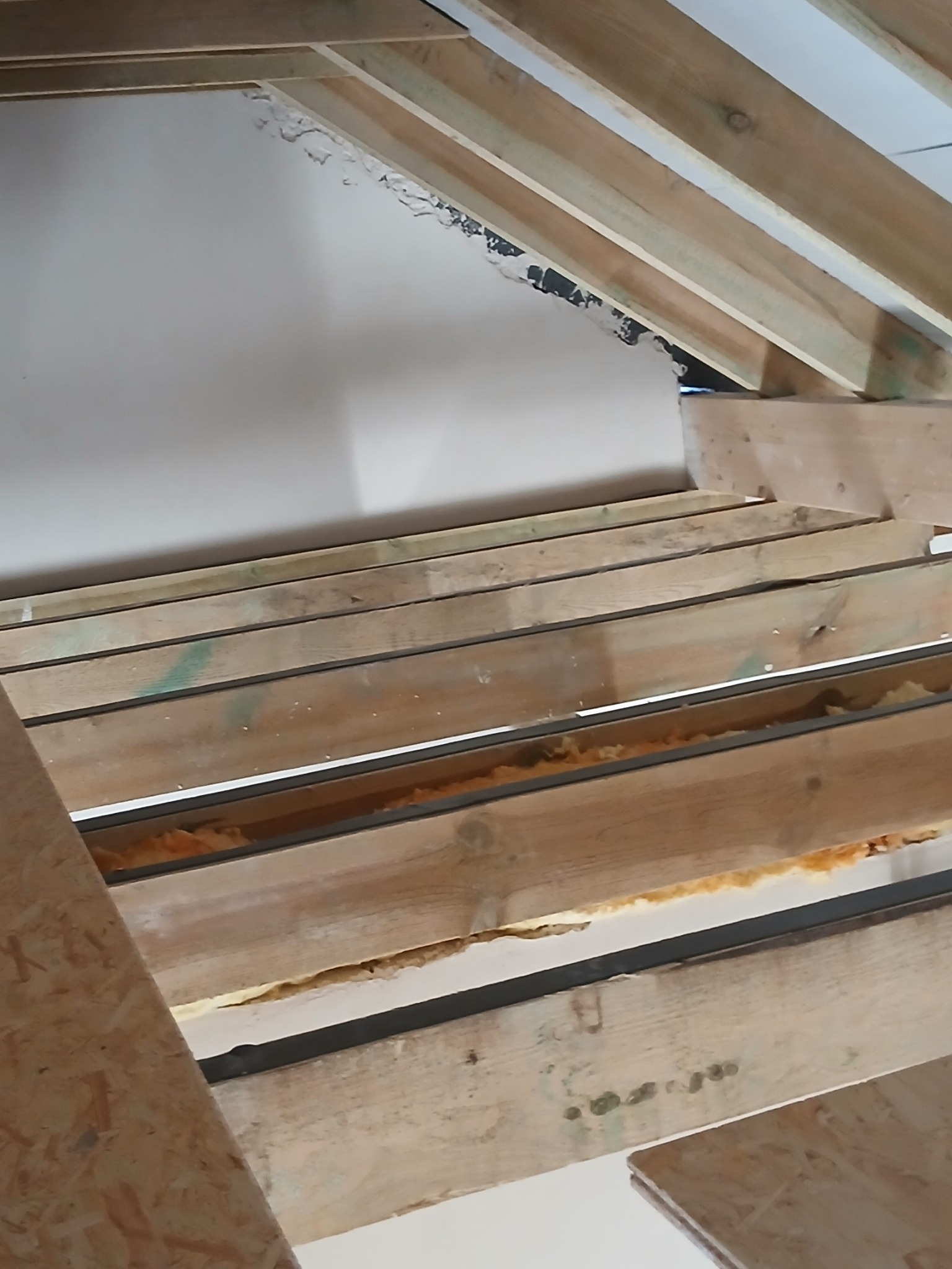 Szkielet drewnianej konstrukcji poddasza z widoczną izolacją, przygotowany do dalszych prac wykończeniowych. Ujęcie z dołu, ukazujące detale belek i materiałów izolacyjnych.