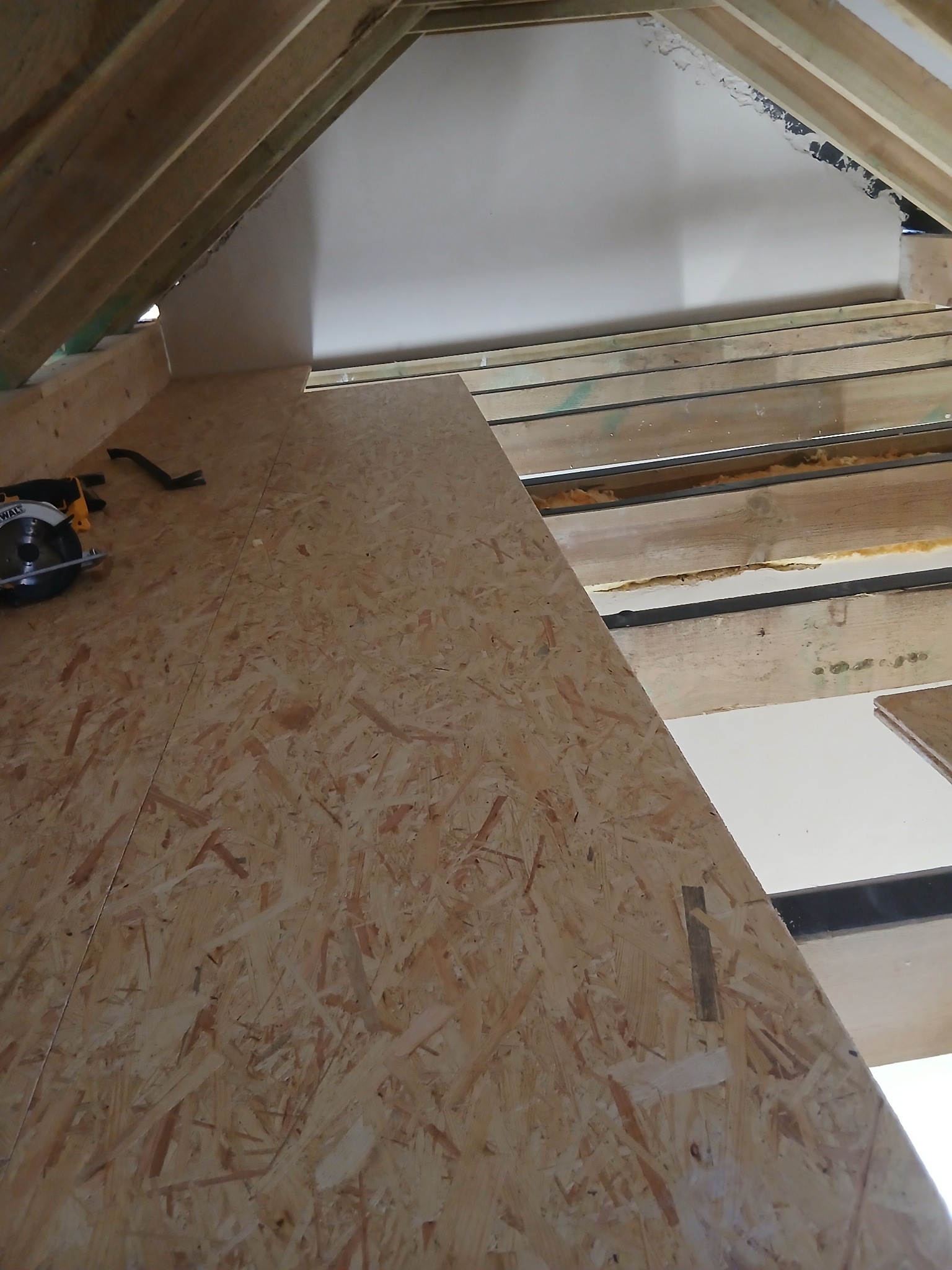 Płyta OSB na poddaszu z widoczną piłą tarczową i konstrukcją dachu. Etap prac wykończeniowych, widoczne ocieplenie między krokwiami.