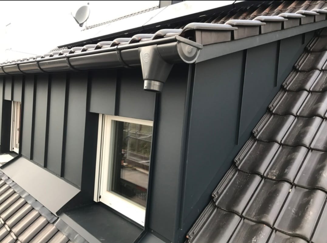 Elewacja z blachy i dachówka ceramiczna, orynnowanie w kolorze antracytowym, Warszawa. Widok na lukarnę i fragment dachu.