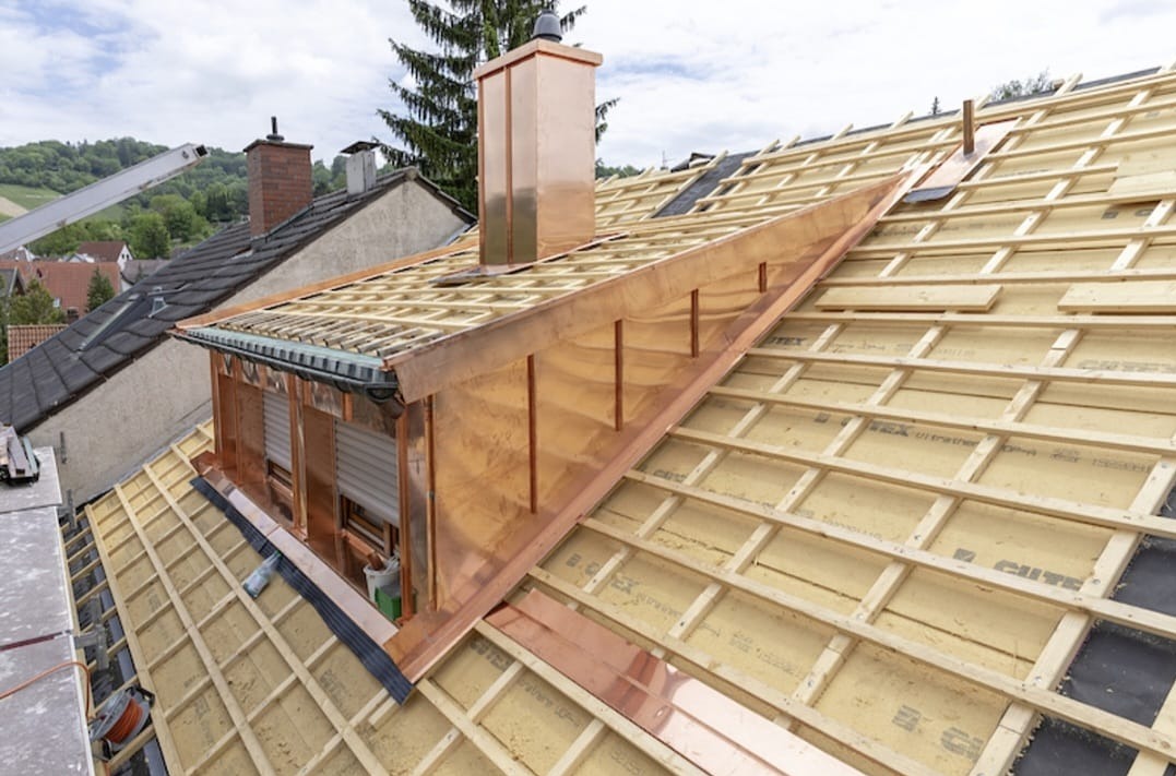 Miedziane obróbki blacharskie na dachu w trakcie budowy, widoczne drewniane łaty i izolacja. Miedziany komin i lukarna. Prace dekarskie w toku.