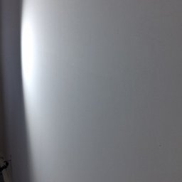 Tomasz kania - Gładka, świeżo pomalowana ściana w odcieniach bieli, z subtelnym cieniowaniem światła z lewej strony. Widoczny fragment podłogi w lewym dolnym rogu.