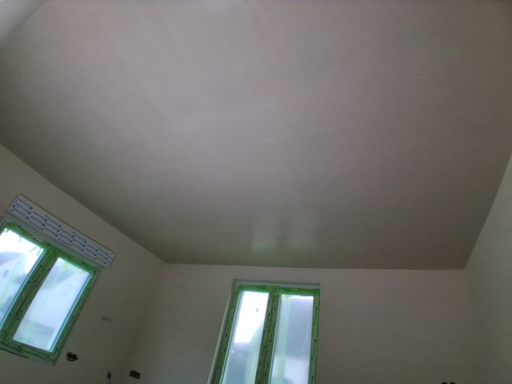 Wnętrze po gładziowaniu: świeżo wygładzony sufit, ściany przygotowane do malowania, okna zabezpieczone folią ochronną. Widok z dołu.