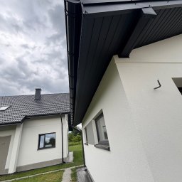 Adri-Tech - Nowoczesny dom z ciemną blachodachówką i rynnami w kolorze antracytu. Widok z dołu, podkreślający estetykę wykończenia dachu i elewacji.