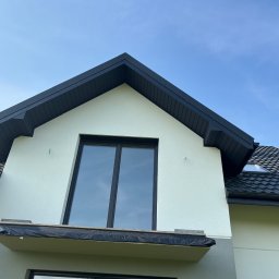 Adri-Tech - Fragment domu z czarną dachówką i obróbkami blacharskimi w kolorze antracytu. Widoczne okno dachowe i balkon z zabezpieczeniem przed zabrudzeniem.