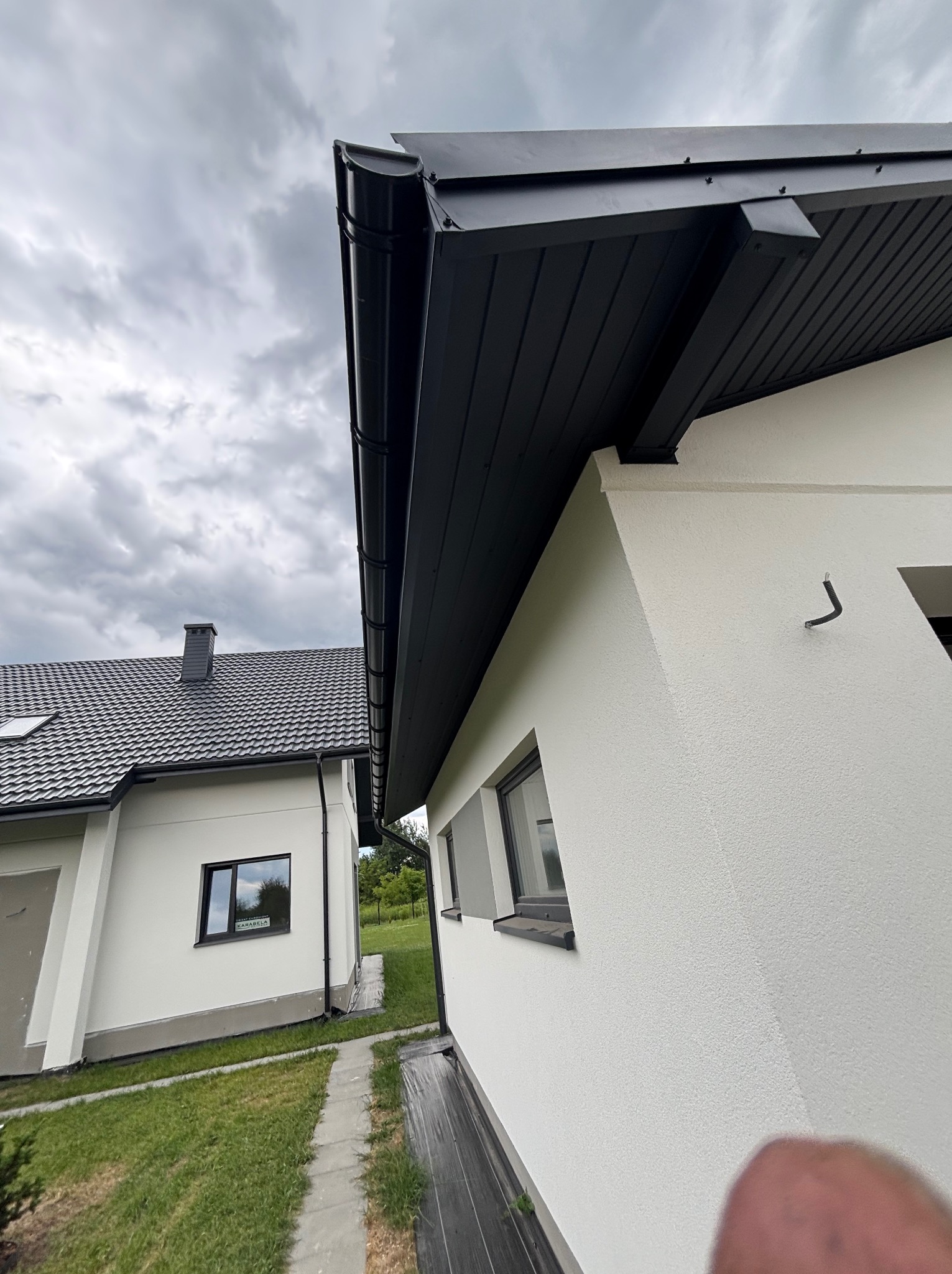 Nowoczesny dom z ciemną blachodachówką i rynnami w kolorze antracytu. Widok z dołu, podkreślający estetykę wykończenia dachu i elewacji.