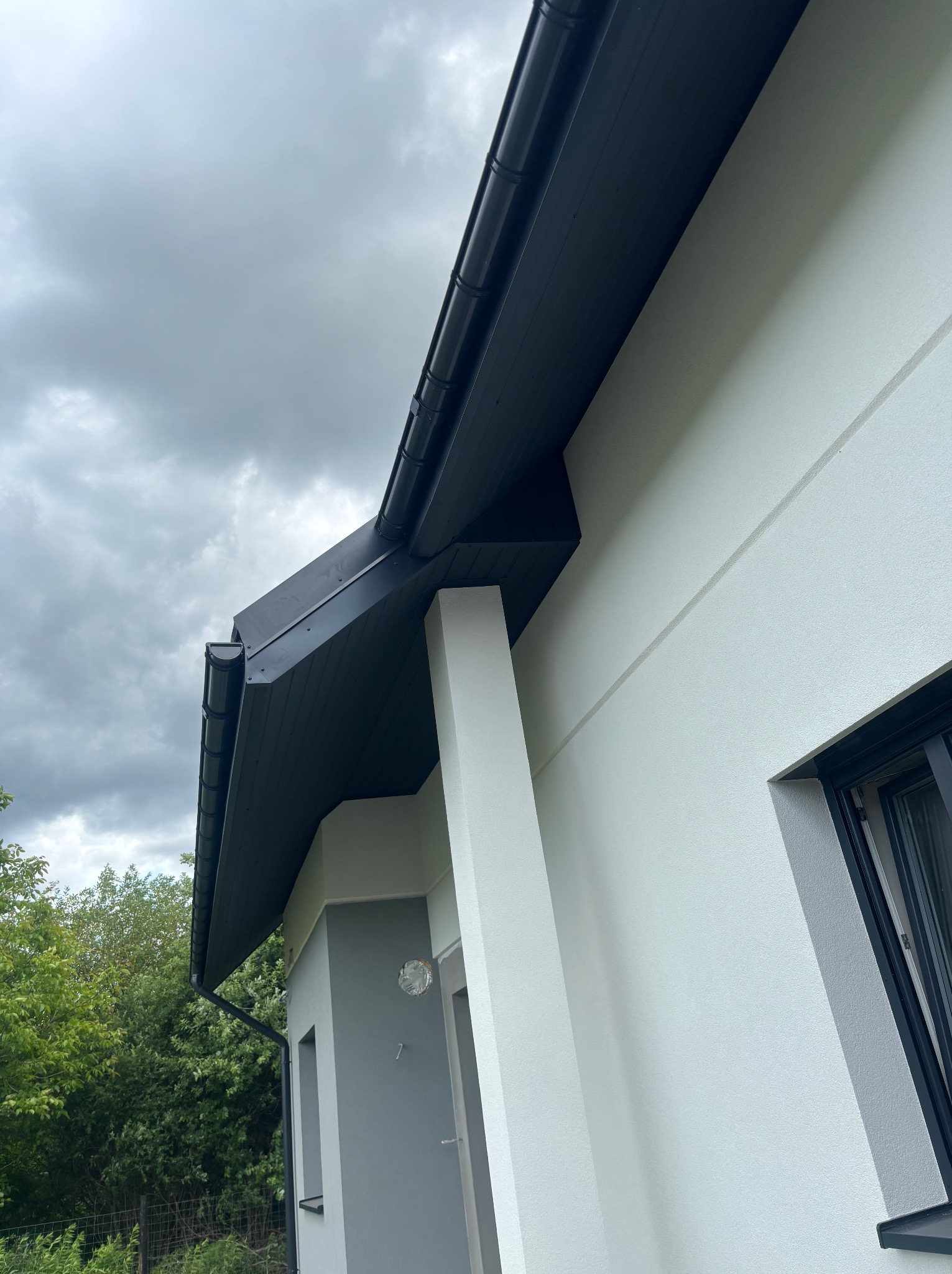 Nowoczesny dom z ciemną blachą na dachu i rynnami. Ujęcie z dołu ukazuje estetyczne wykończenie i dbałość o detale.