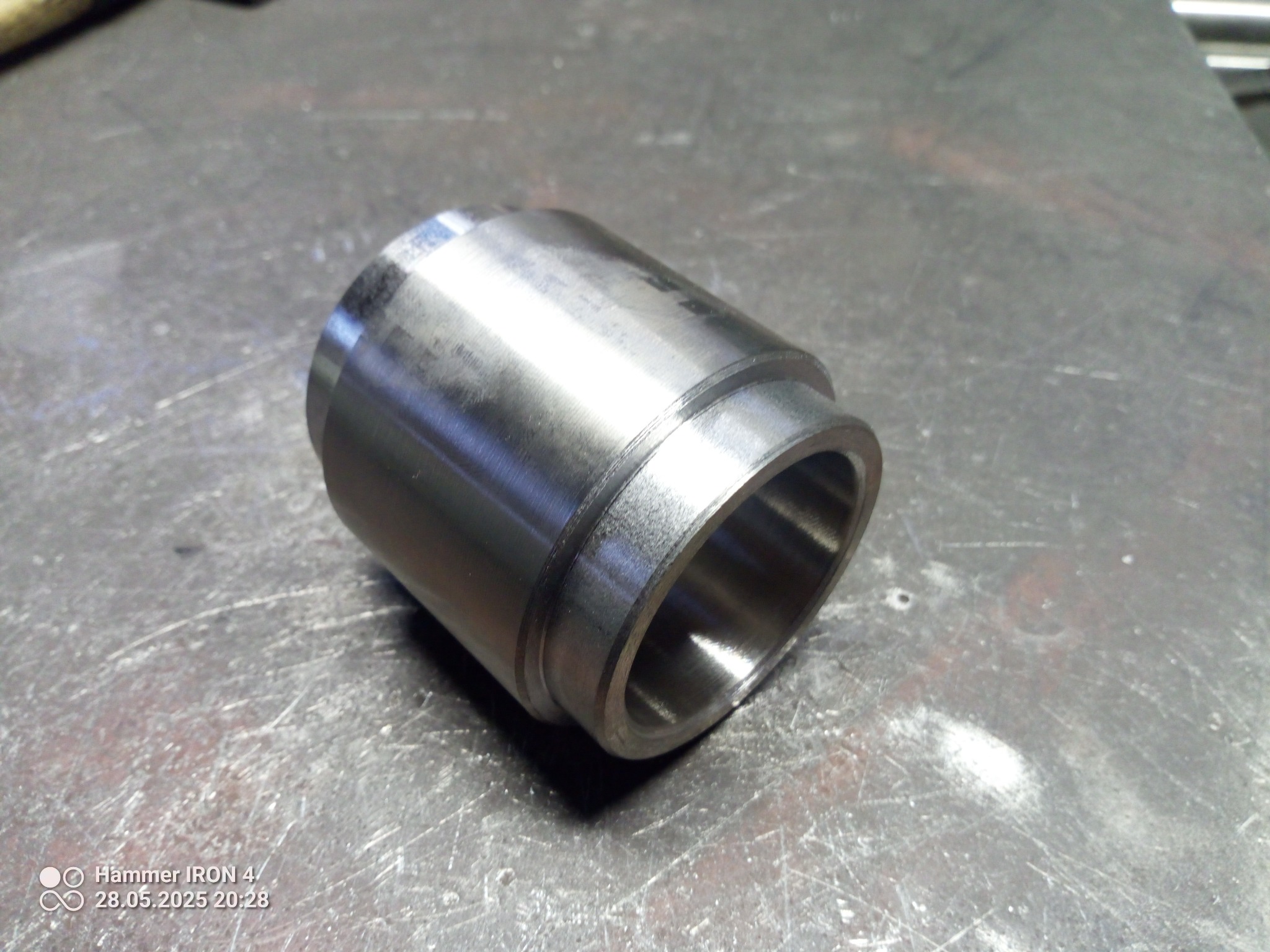 Metalowy cylinder z rantem na szorstkiej powierzchni, widoczne ślady obróbki, ostre światło podkreśla detale, minimalizm i precyzja wykonania.