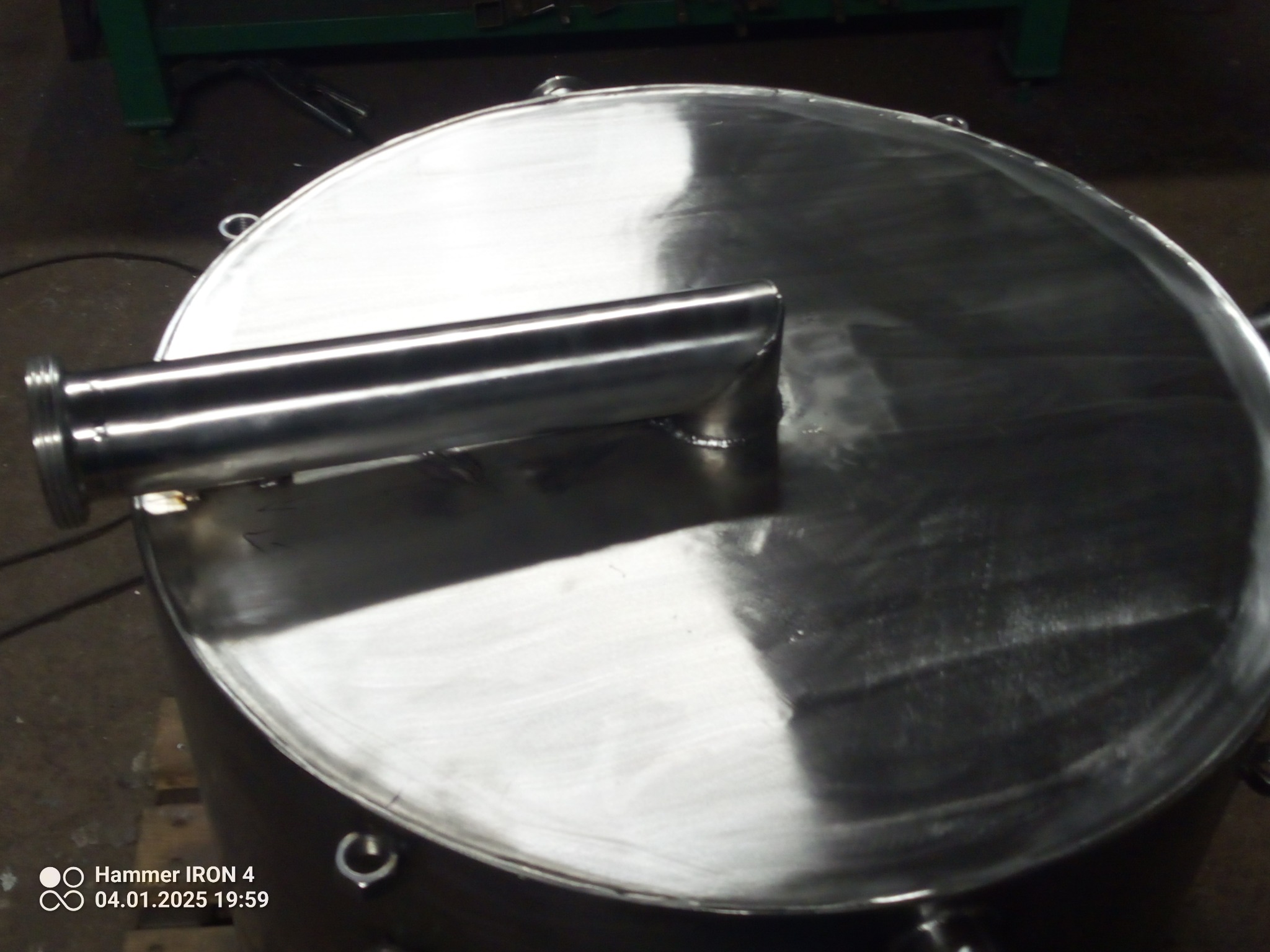 Spawana konstrukcja ze stali nierdzewnej: okrągły zbiornik z rurą. Widoczne ślady spawania i polerowania, metaliczny połysk. Detal wykonany w warsztacie.